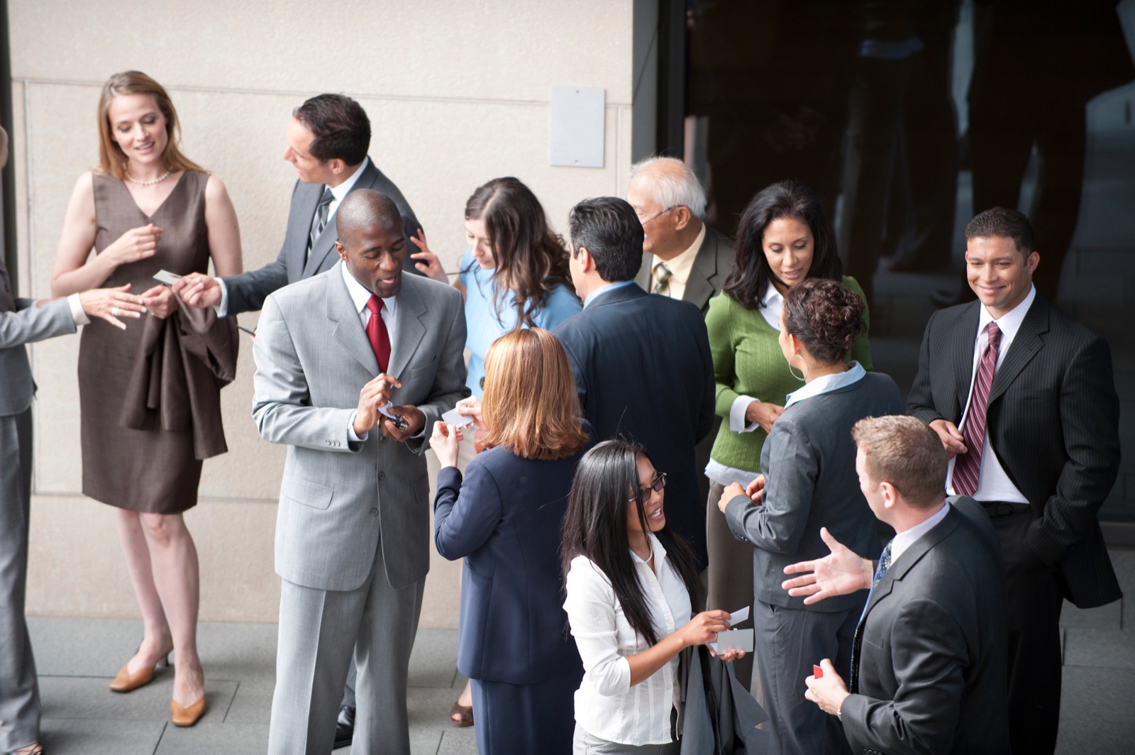 Business professionals exchanging cards in a networking event. The setting is a modern office lobby. Attendees are smiling and engaged.